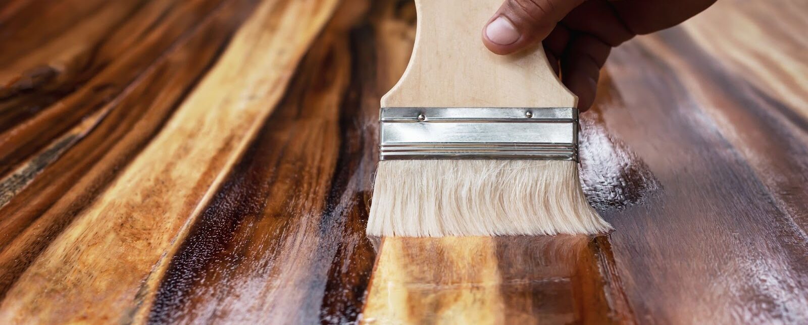 A brush applying wood stain to a beautiful hardwood floor demonstrating a step of how to stain hardwood floors.